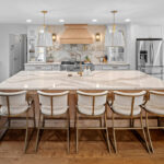 White kitchen with marble counter tops and backsplash with stained wood hood.