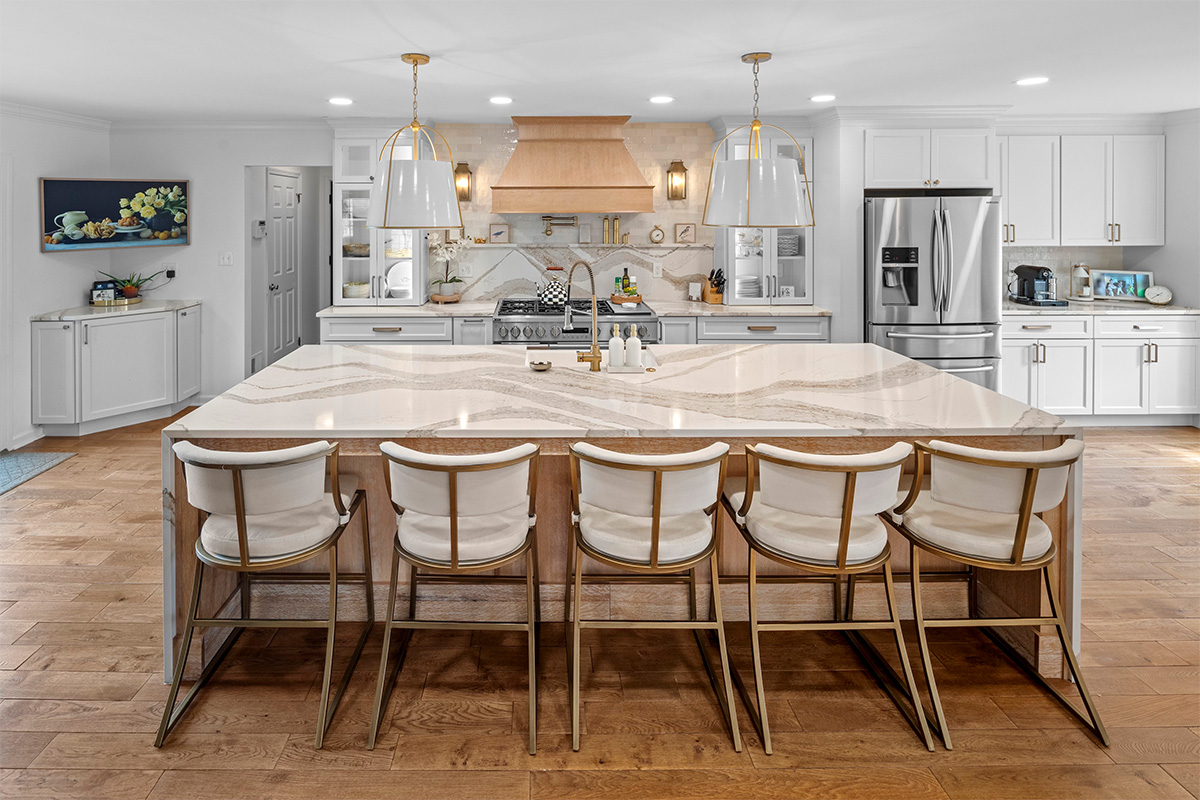 White kitchen with marble counter tops and backsplash with stained wood hood.