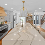 White kitchen with marble counter tops and backsplash with stained wood hood.