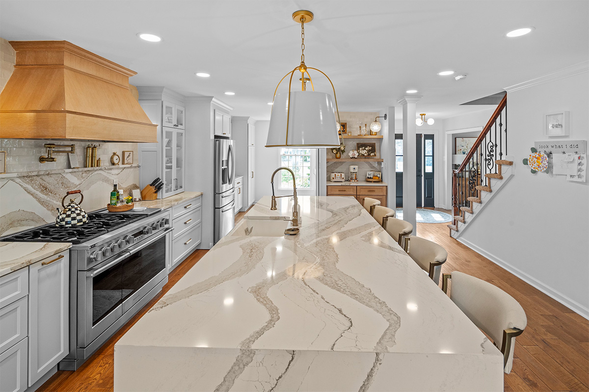 White kitchen with marble counter tops and backsplash with stained wood hood.