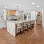 White kitchen with marble counter tops and backsplash with stained wood hood.