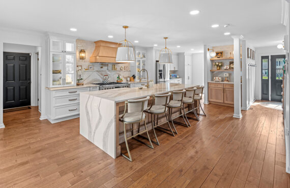 White kitchen with marble counter tops and backsplash with stained wood hood.