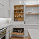 White kitchen perimeter cabinets with doors open showing shelves and roll tray storage within.