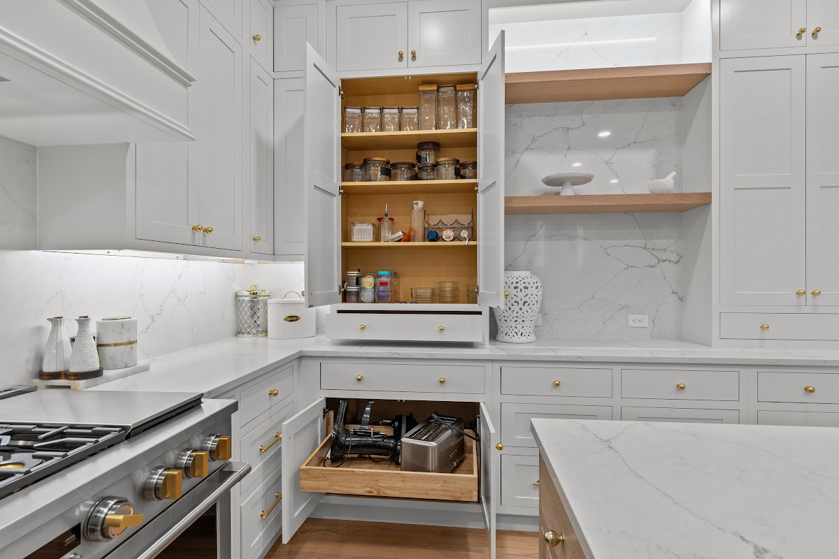 White kitchen perimeter cabinets with doors open showing shelves and roll tray storage within.