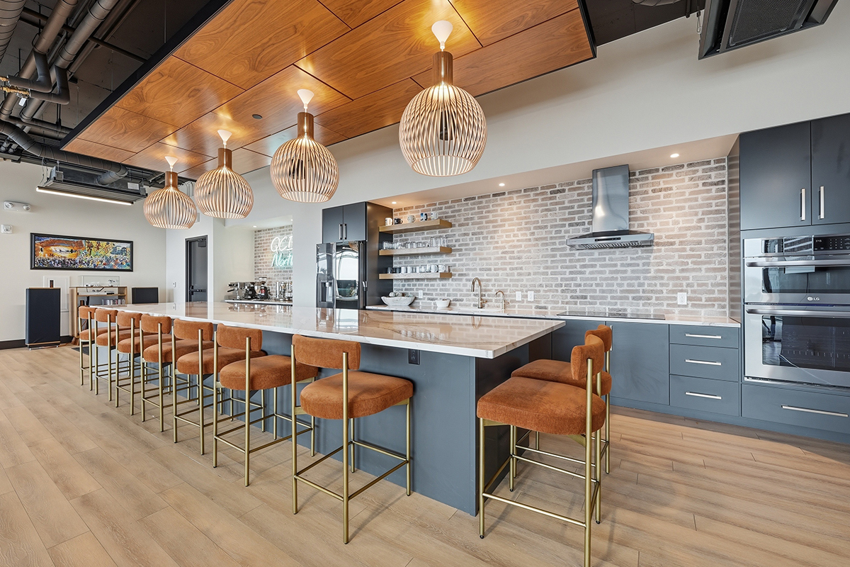 Gray painted office breakroom kitchen with long island with many seats.