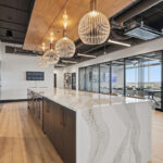 Gray painted office breakroom kitchen with long island with many seats.