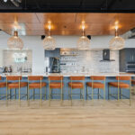 Gray painted office breakroom kitchen with long island with many seats.