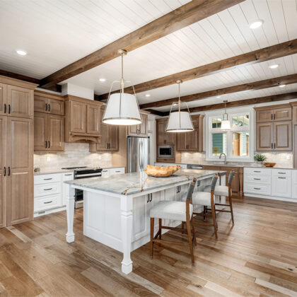 Brown-stained and white kitchen perimeter and island cabinets. Island includes decorative legs and seating.
