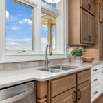 Brown-stained and white kitchen cabinets with sink by window.