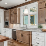 Brown-stained and white kitchen cabinets with sink by window.
