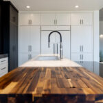 Modern white kitchen cabinets and a wood countertop near the sink in the island