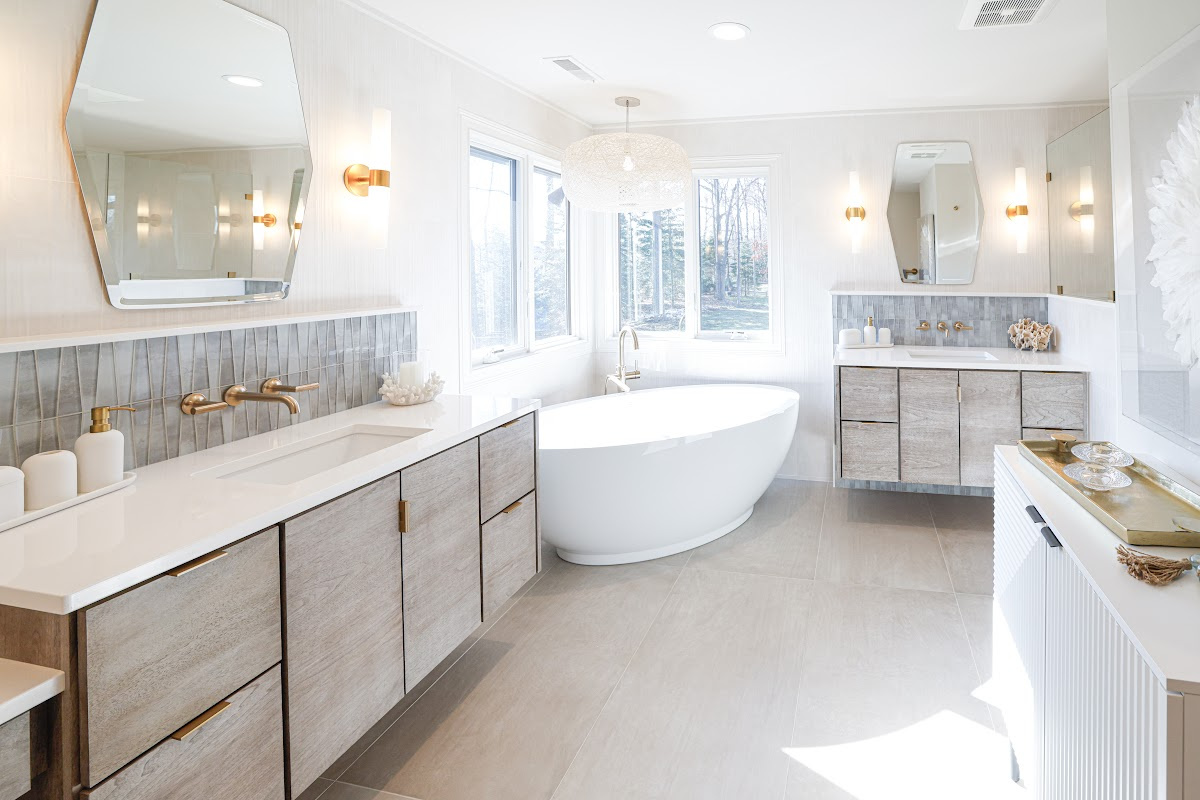 Large master bathroom with 2 vanity areas with light Montana stain, powder desk and large free-standing tub in the corner below large windows.