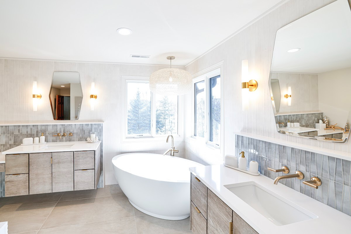 Large master bathroom with 2 vanity areas with light Montana stain, powder desk and large free-standing tub in the corner below large windows.