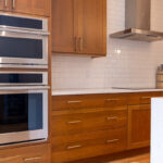 Cherry kitchen cabinets with a red Sienna stain. view shows stainless steel appliances on hood.