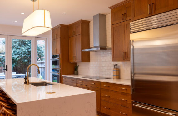 Cherry kitchen cabinets with a red Sienna stain. view shows stainless steel appliances on hood.