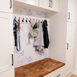 White mudroom bench with cabinet storage and hanging coats on hooks