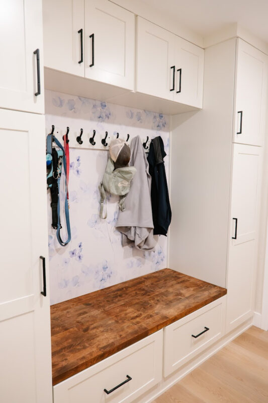 White mudroom bench with cabinet storage and hanging coats on hooks