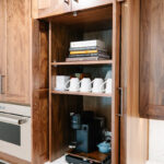 Brown-stained coffee center cabinet with open pocket doors showing coffee maker and mugs