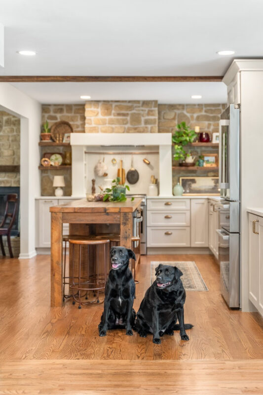 Old World style kitchen with Light Mocha-painted perimeter and a custom wood island in a mid-brown stain. 2 black labs are sitting at the front of the island.