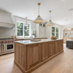 White and light brown kitchen cabinets. View is from the front of the island facing the hood and window.