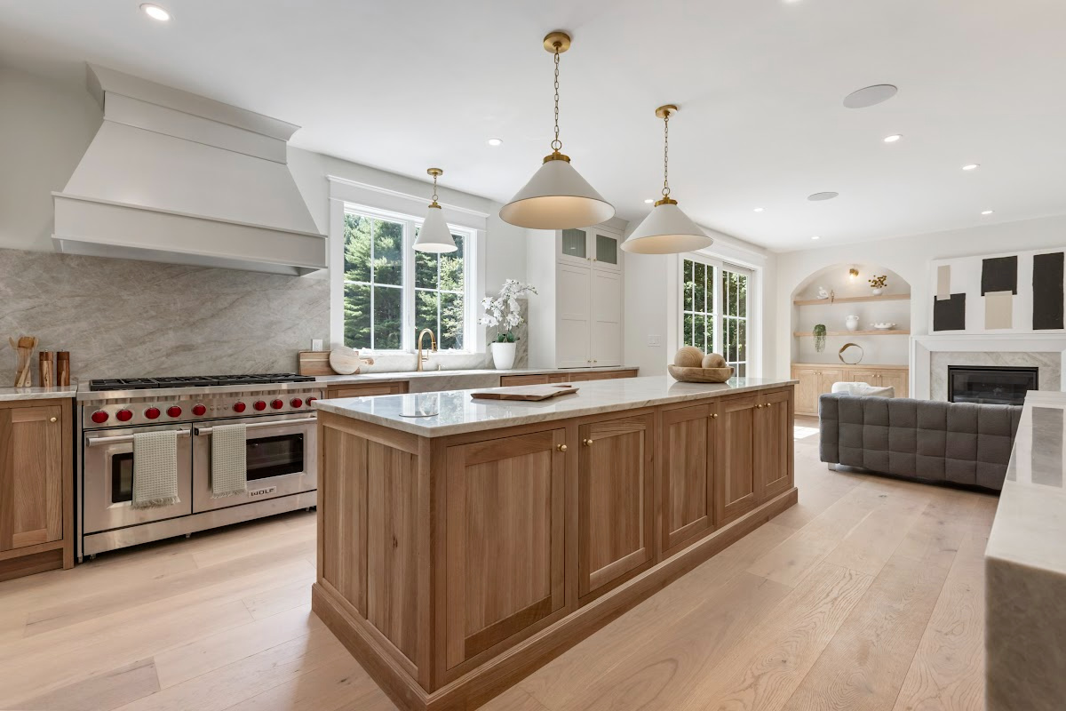 White and light brown kitchen cabinets. View is from the front of the island facing the hood and window.