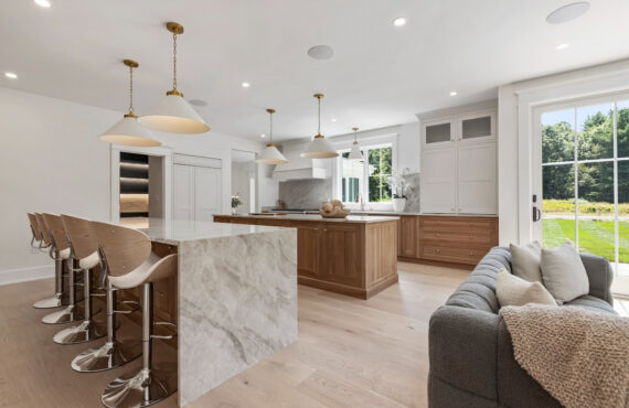 White and light brown kitchen cabinets. View is from the front of the island facing the hood and window.