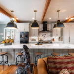 Painted Oyster primary kitchen cabinets with black appliances and green island.