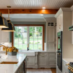Painted Oyster primary kitchen cabinets with black appliances and green island.