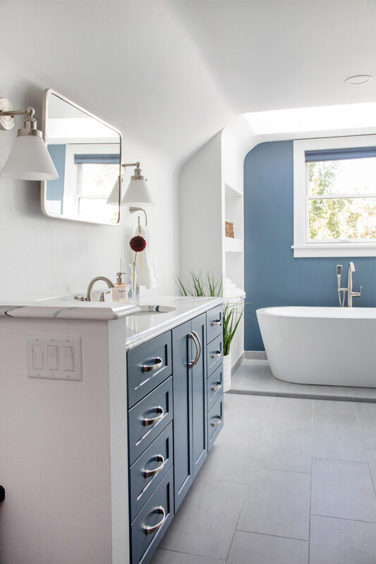 Bathroom with blue cabinetry and accent wall with white freestanding tub