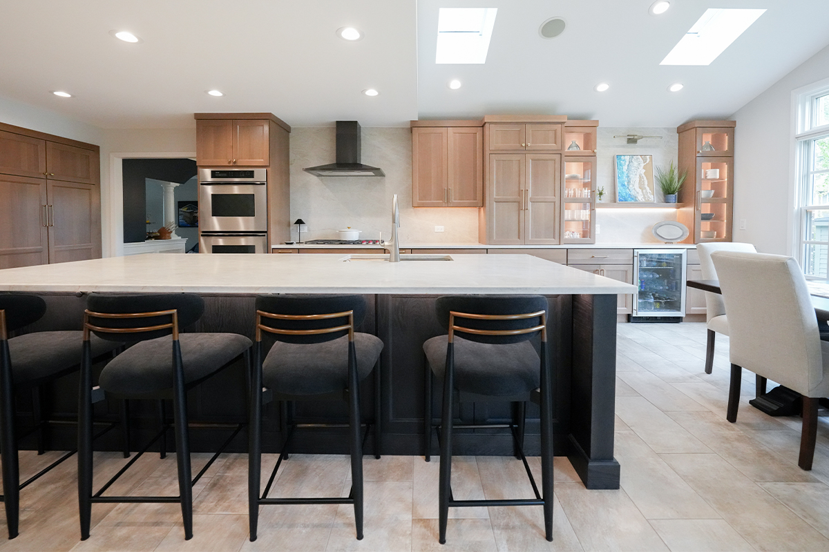 Open kitchen with perimeter cabinets in Sable stain on rift white oak and a dark island in Midnight stain.