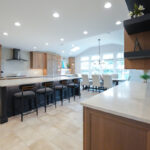Open kitchen with perimeter cabinets in Sable stain on rift white oak and a dark island in Midnight stain.