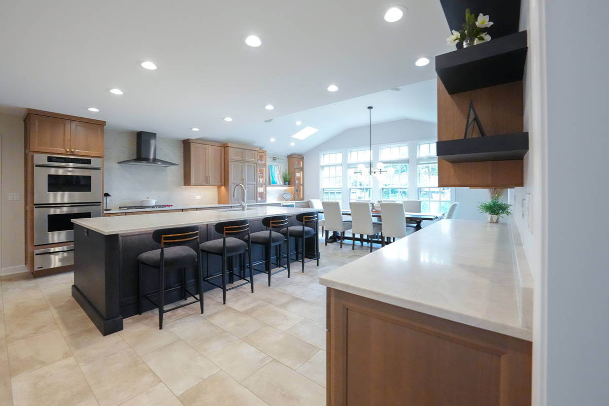 Open kitchen with perimeter cabinets in Sable stain on rift white oak and a dark island in Midnight stain.