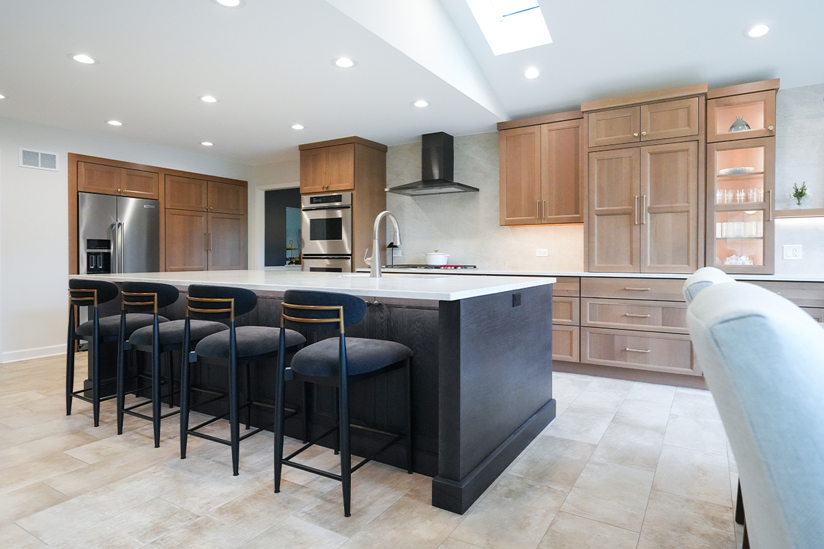 Open kitchen with perimeter cabinets in Sable stain on rift white oak and a dark island in Midnight stain.