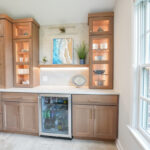 Kitchen cabinets in light brown stain with wine fridge below the counter and glass door cabinets above.