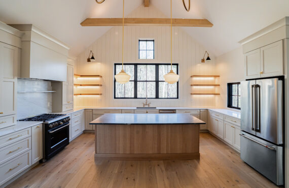 Light beige kitchen cabinets with hood and floating shelves. Also, visible is an island in rift white oak.
