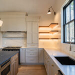 Light beige kitchen cabinets with hood and floating shelves.