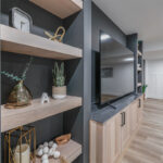 Entertainment center with large tv above light stained cabinets and open shelving on each side.