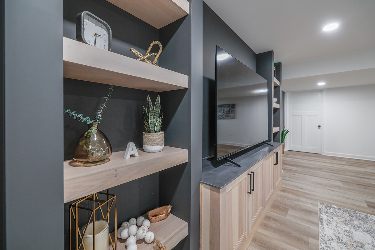Entertainment center with large tv above light stained cabinets and open shelving on each side.
