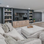 Entertainment center with large tv above light stained cabinets and open shelving on each side.