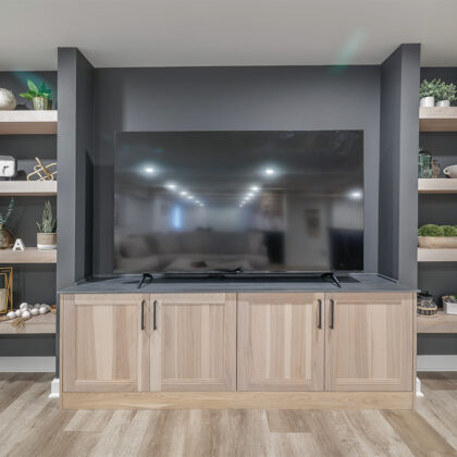 Entertainment center with large tv above light stained cabinets and open shelving on each side.