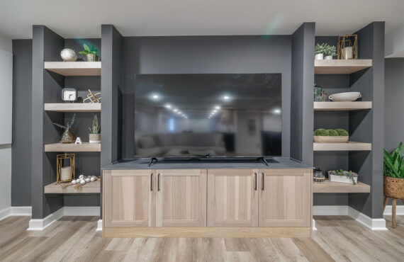 Entertainment center with large tv above light stained cabinets and open shelving on each side.