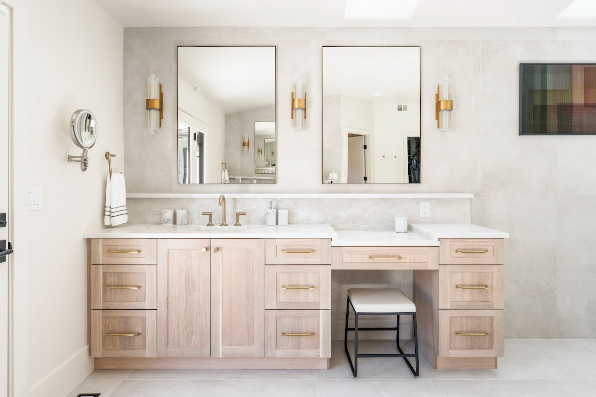 Light stained bathroom vanity with powder desk and two contemporary mirrors.