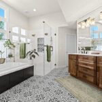Bright and airy bathroom with several windows above the tub and warm brown stained double sink vanity with large mirror above.