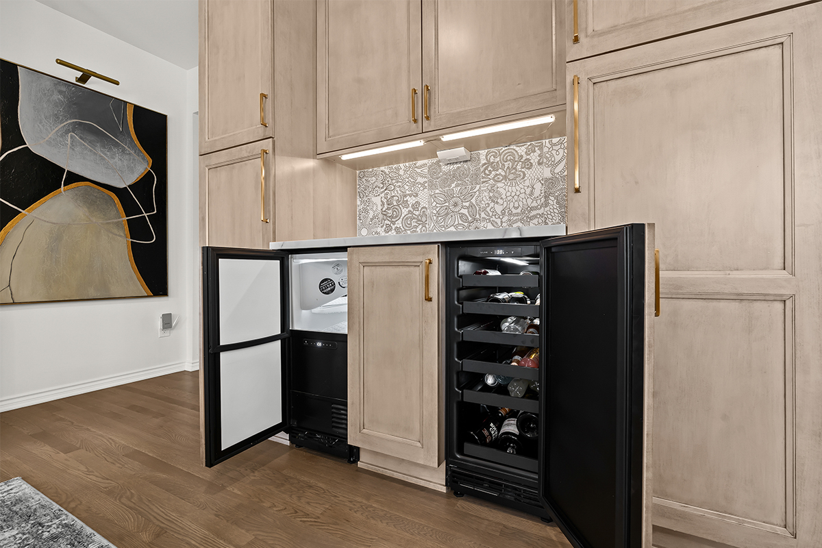 Kitchen cabinets with light brown stain and black under counter ice maker and wine fridge.