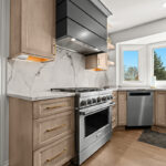 Kitchen cabinets with light brown stain. Shows a gray painted wood hood and stainless steel oven.