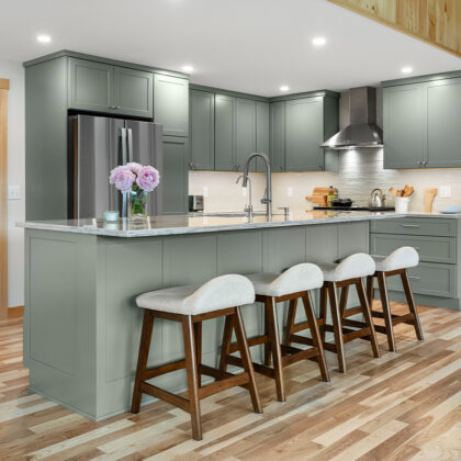 Green kitchen cabinets with island seating and light brown wood floors.