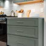 Green kitchen cabinets with island seating and light brown wood floors.