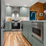 Green kitchen cabinets with island seating and light brown wood floors.
