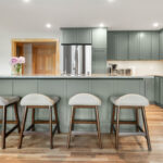 Green kitchen cabinets with island seating and light brown wood floors.