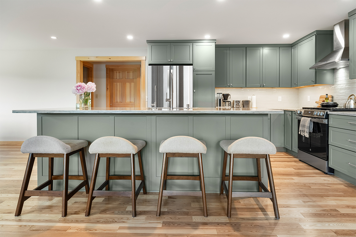 Green kitchen cabinets with island seating and light brown wood floors.